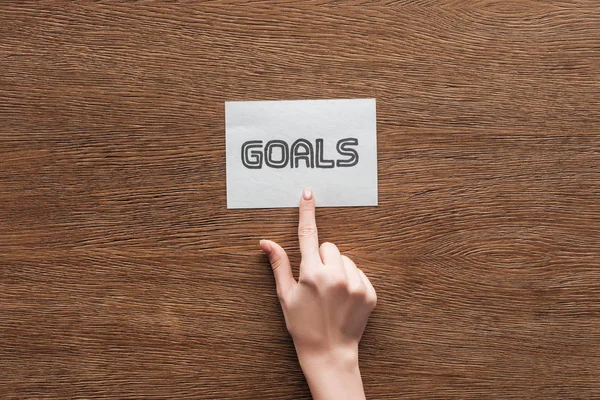 Partial view of woman pointing at  'goals' lettering on card with wooden background — Stock Photo