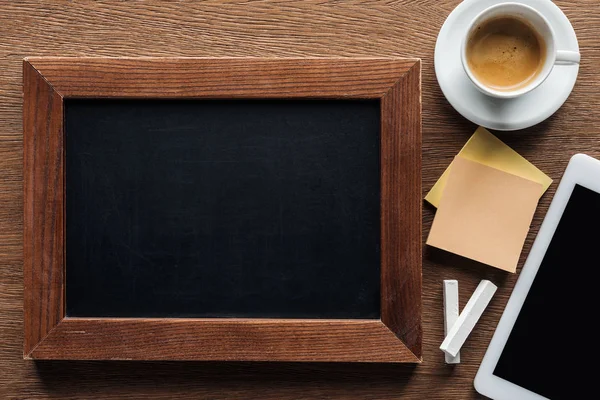 Draufsicht auf leere Kreidetafel mit digitalem Tablet und Kaffee auf Holzgrund — Stockfoto