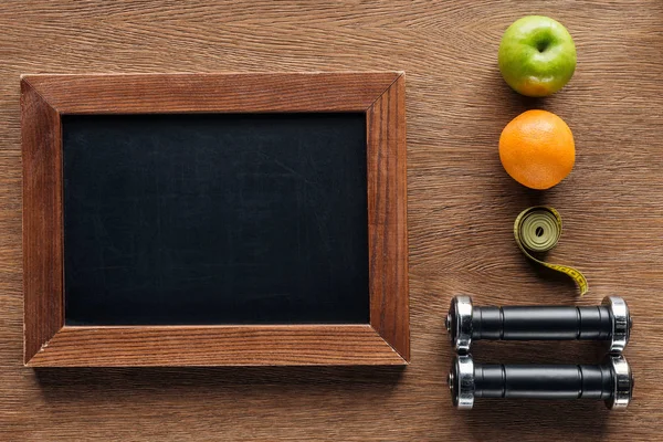 Vista superior de pizarra de madera en blanco, frutas, pesas y cinta métrica, dieta y concepto de estilo de vida saludable - foto de stock