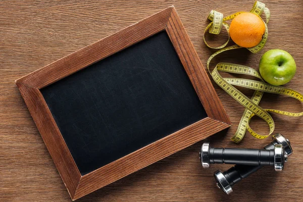 Vue du dessus du tableau à craie en bois blanc, des fruits, des haltères et du ruban à mesurer, du régime alimentaire et du concept de style de vie sain — Photo de stock