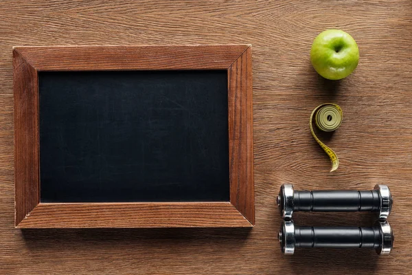 Vista superior da placa de giz de madeira em branco, maçã, halteres e fita métrica, dieta e conceito de estilo de vida saudável — Fotografia de Stock