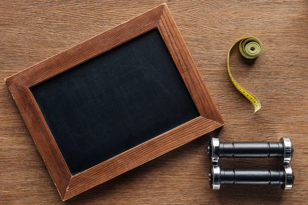 Blank wooden chalk board, measuring tape and dumbbells, dieting and healthy lifesyle concept — Stock Photo