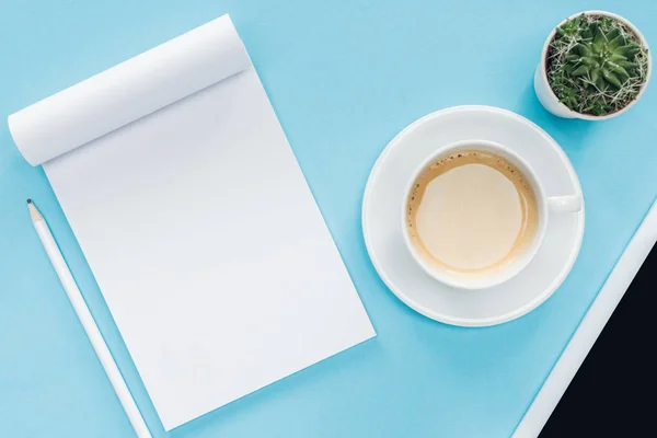 Vista superior de notebook em branco com lápis, xícara de café no fundo azul — Fotografia de Stock