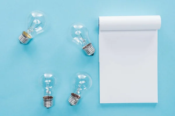 Top view of blank notebook with light bulbs on blue background, having idea concept — Stock Photo