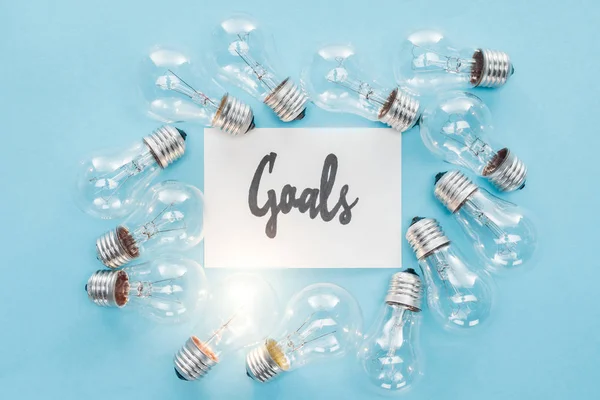 Top view of 'goals' word written in cursive on card surrounded by circle of light bulbs on blue background, goal setting concept — Stock Photo