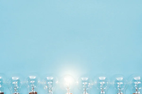 Top view of light bulbs in row and one of them glowing on blue background, having new idea concept — Stock Photo