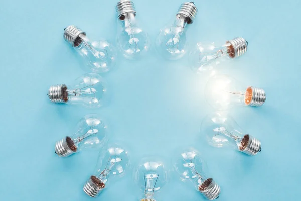 Top view of light bulbs in circle and one of them glowing on blue background, having new idea concept — Stock Photo