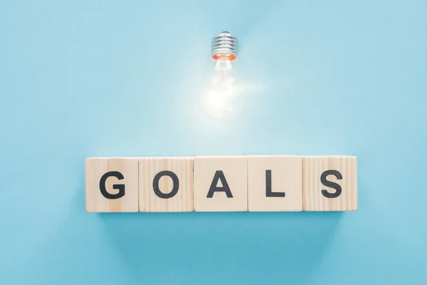 Top view of glowing light bulb over 'goals' word made of wooden blocks on blue background, goal setting concept — Stock Photo