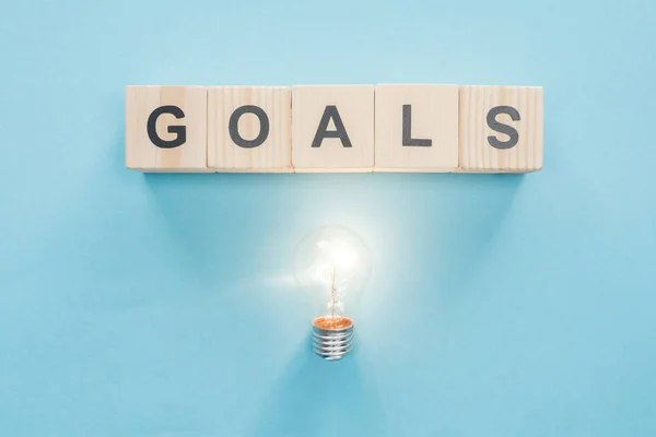 Top view of glowing light bulb under 'goals' word made of wooden blocks on blue background, goal setting concept — Stock Photo