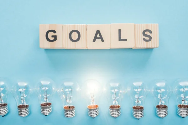 Top view of glowing light bulbs under 'goals' word made of wooden blocks on blue background, goal setting concept — Stock Photo