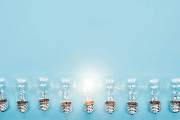 Vista superior de lâmpadas na fileira e um deles brilhando no fundo azul, tendo novo conceito de ideias — Fotografia de Stock