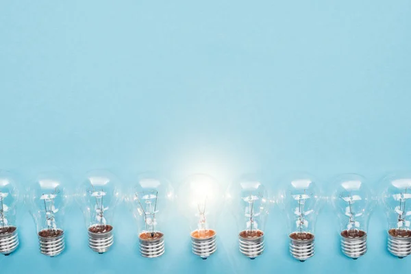 Vista dall'alto di lampadine in fila e uno di loro incandescente su sfondo blu, avendo nuove idee concetto — Foto stock