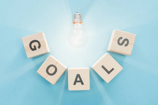 Top view of glowing light bulb over 'goals' word made of wooden blocks on blue background, goal setting concept — Stock Photo