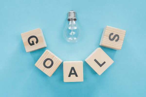 Top view of light bulb over 'goals' word made of wooden blocks on blue background, goal setting concept — Stock Photo