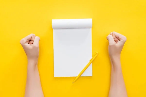 Ausgeschnittene Ansicht einer entschlossenen Person mit Fäusten auf dem Tisch, die an einem leeren Notizbuch arbeitet — Stockfoto