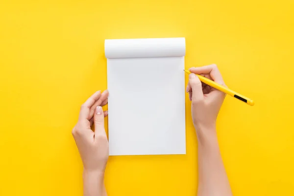 Vista parcial pessoa segurando caneta sobre notebook em branco no fundo amarelo — Fotografia de Stock