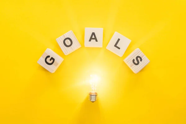 Top view of glowing light bulb under 'goals' word made of wooden blocks on yellow background, goal setting concept — Stock Photo