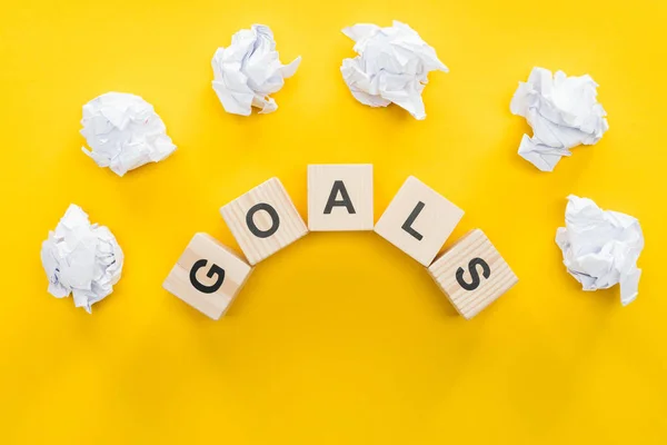 Crumbled paper balls over 'goals' word made of wooden blocks on yellow background, goal setting concept — Stock Photo
