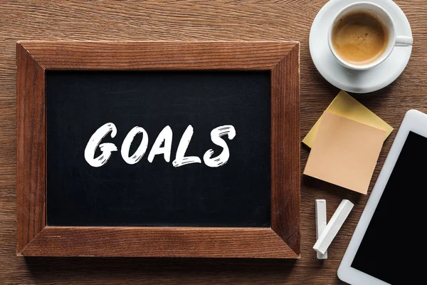 Top view of 'goals' lettering on chalk board with coffee and digital tablet on wooden background — Stock Photo