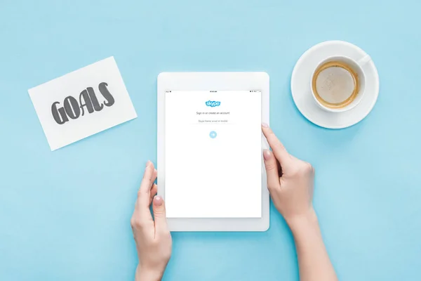 Corte vista da fêmea usando tablet digital com skype aplicativo na tela, metas lettering no cartão e café no fundo azul — Fotografia de Stock