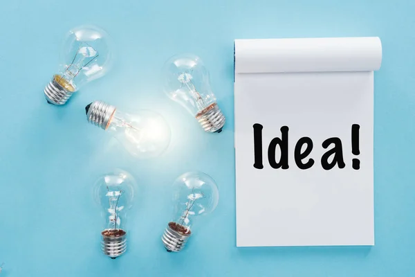 Notebook com 'ideia' palavra perto de lâmpadas com um brilhante, tendo novas ideias conceito — Fotografia de Stock