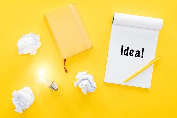 Notebook with 'idea' word, crumbled paper balls and glowing light bulb, having new ideas concept — Stock Photo