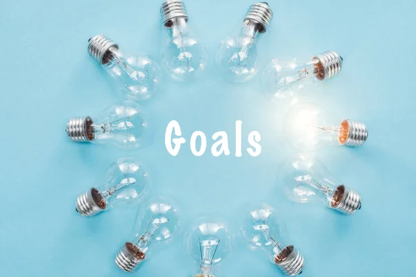 Circle of light bulbs with glowing one surronding 'goals' word on blue, goal setting concept — Stock Photo