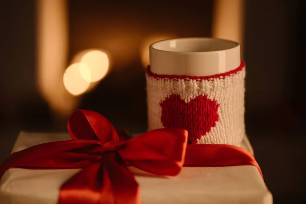 Present and knitted mug with heart symbol on blurred background — Stock Photo