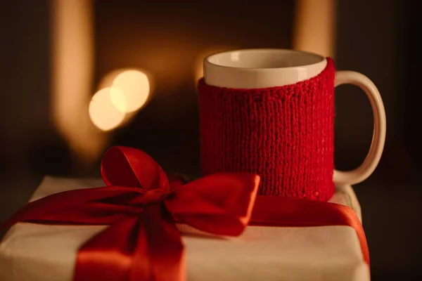 Knitted mug and present with bow on blurred background — Stock Photo