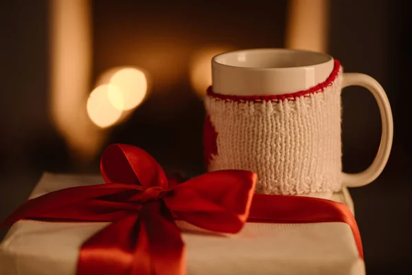 Present with bow and knitted mug on blurred background — Stock Photo