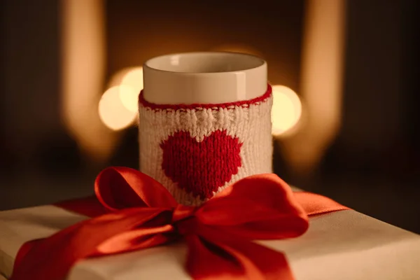 Present and knitted mug with heart symbol on blurred background — Stock Photo