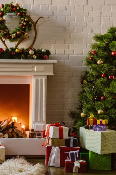 Sapin de Noël avec décorations festives et coffrets cadeaux près de la cheminée avec bois de chauffage dans le salon — Photo de stock