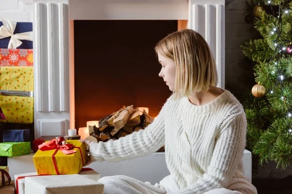 Young woman putting gift box near fireplace with firewood — Stock Photo
