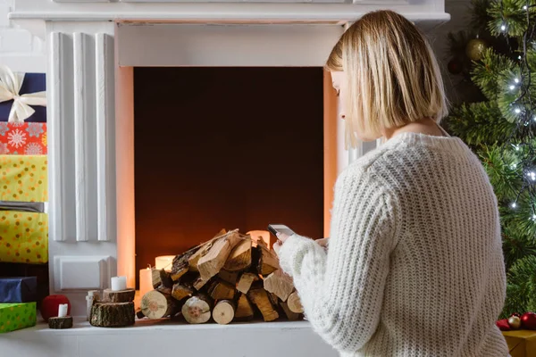 Young woman sitting near fireplace with firewood — Stock Photo