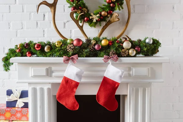 Corona de Navidad con decoraciones, medias y cuernos de ciervo sobre chimenea mantel - foto de stock