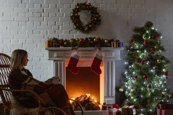 Young woman on wicker rocking chair holding cup of coffee in living room decorated for christmas — Stock Photo