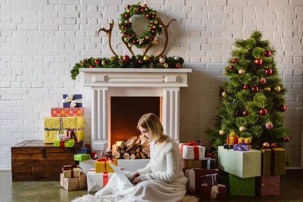 Mujer joven sentada y usando el ordenador portátil en la sala de estar decorada para Navidad - foto de stock