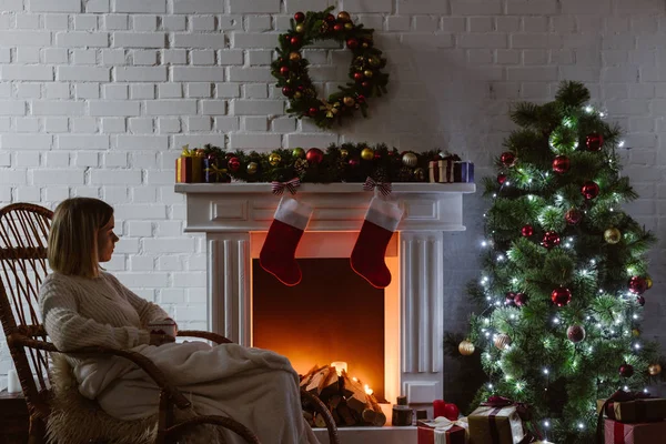 Mujer joven sentada en mecedora de mimbre en la sala de estar decorada para Navidad - foto de stock