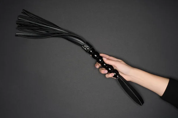 Cropped view of female hand holding flogging whip isolated on grey — Stock Photo