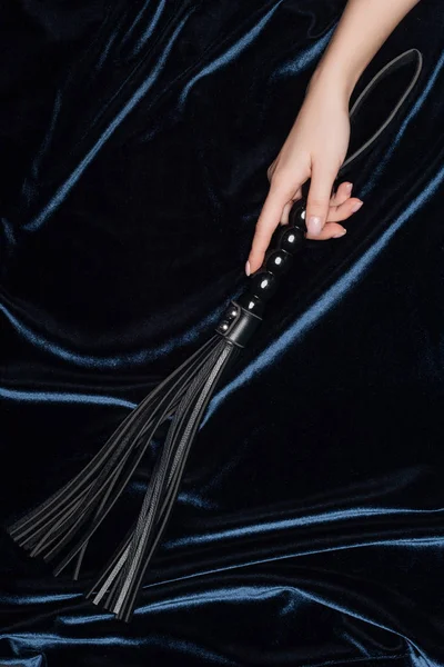 Cropped view of female hand holding flogging whip with shiny velvet cloth at background — Stock Photo