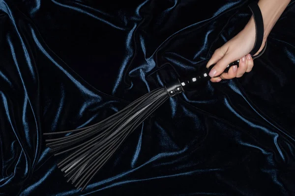 Primer plano de la mano femenina celebración látigo azotes con tela de terciopelo oscuro en el fondo - foto de stock