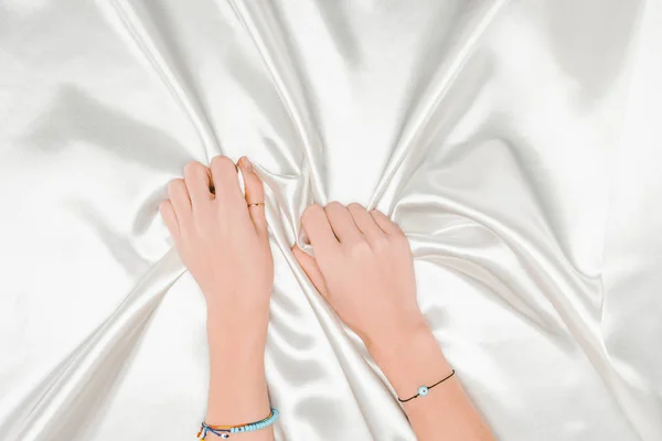 Vue de dessus des mains féminines tenant fermement brillant tissu satiné blanc — Photo de stock
