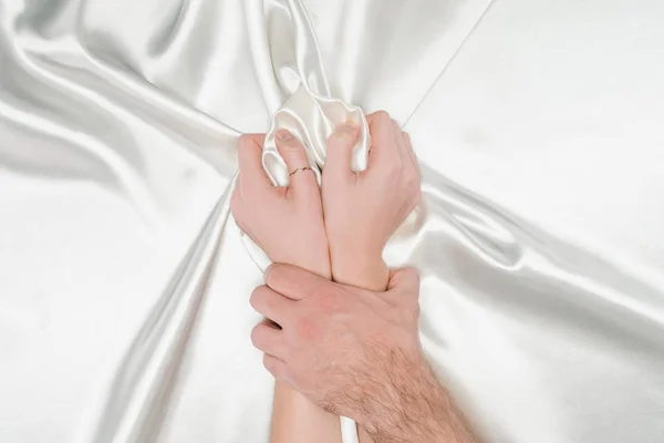 Male hand tightly holding female hands on silk white cloth — Stock Photo