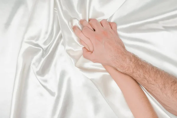 Top view of male hand tightly holding female hand on silk white cloth — Stock Photo