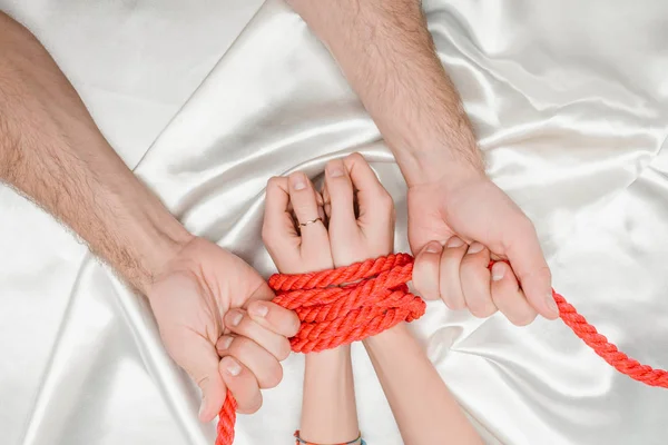 Vue de dessus des mains masculines serrant étroitement les mains féminines avec corde rouge — Photo de stock