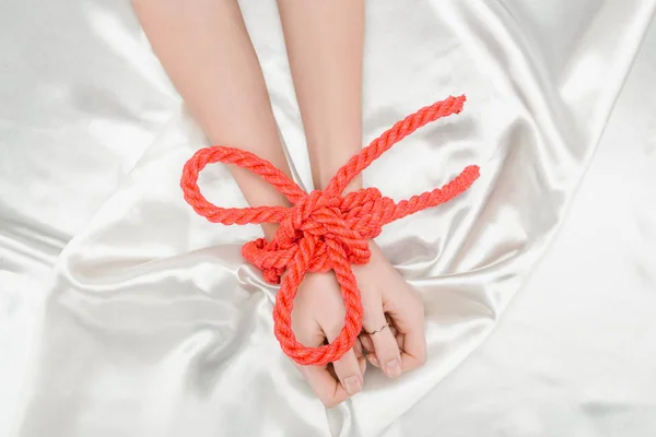 Cropped view of female hands bounded with bright red rope on satin cloth — Stock Photo