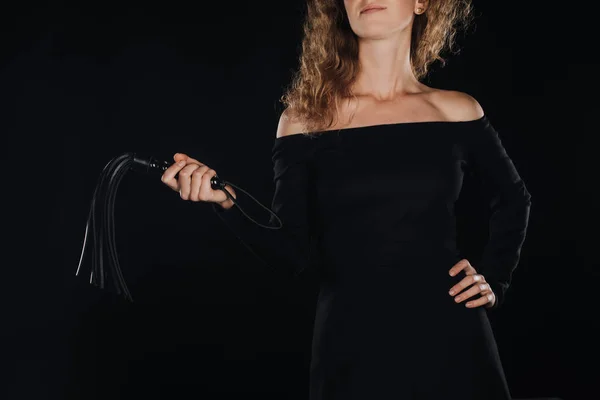 Vista parcial de la mujer sosteniendo látigo azotes de cuero en la mano aislado en negro - foto de stock