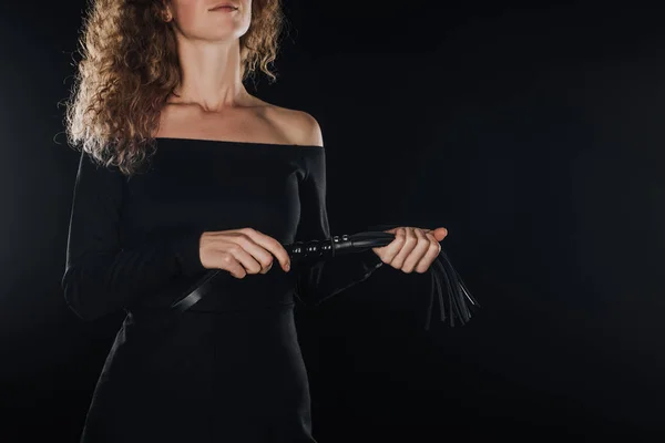 Взрослая женщина держит кожаный кнут, изолированный на черном — стоковое фото