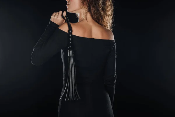 Vista posterior de la mujer adulta sosteniendo látigo azotes aislado en negro - foto de stock