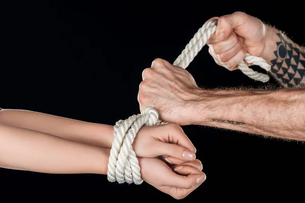 Cropped view of man tying rope on female hands isolated on black — Stock Photo